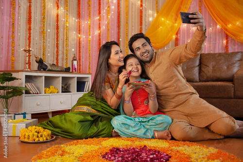 Young Indian couple with their daughter celebrating diwali at home - Indian festival, hindu festival. Indian festival Diwali celebration - Small nuclear family decorating the house, taking selfie