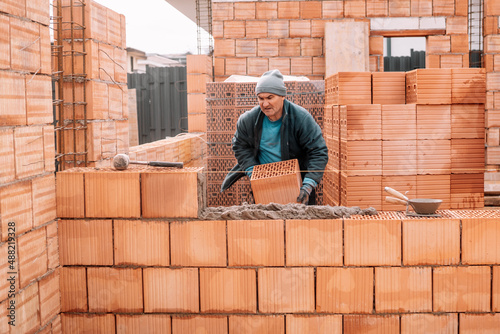 Industrial male bricklayer installing bricks on construction site. Construction site, walls building © aboutmomentsimages