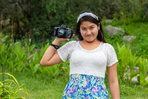 
chica hermosa con cámara sosteniendo en la mano,Sonriente mujer con cara hermosa y de pie en el aire libre,naturaleza,
 photo