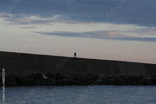 Foto poetica di una persona che cammina in solitaria sul molo del porto in riva al mare al crepuscolo 