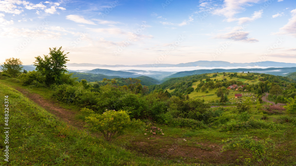 carpathian rural landscape in spring at sunrise. trees on the grassy hills rolling in to the distant valley in morning light. fluffy cloud formations on the sky. beautiful nature background
