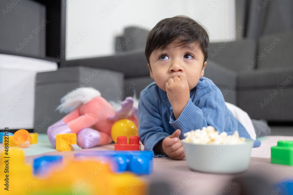 two years old mexican baby boy eating popcorn on messy room