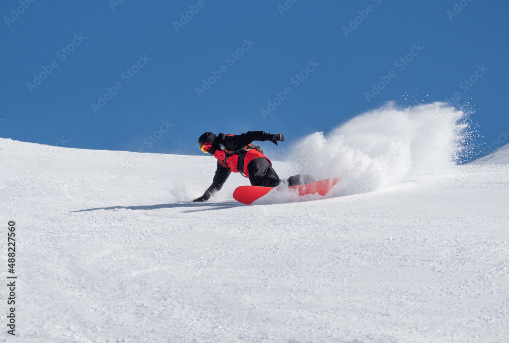 Active man carving on snowboard on ski slope at sunny winter day