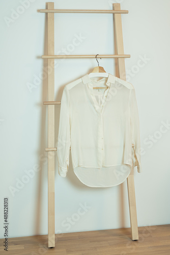 Classic white silk women blouse hanging on wooden hanger ladder.