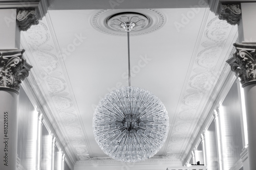 Large ceiling glass round chandelier in the foyer of room with columns.
