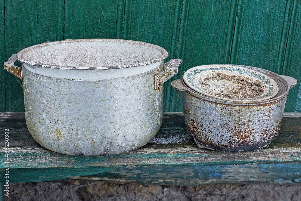 old dishes from dirty bowls and pans stand on a gray table against a green wall