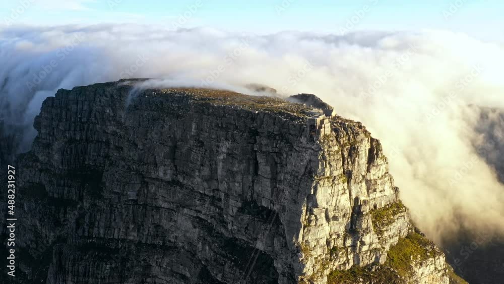 Backward tracking aerial shot looking down at a massive bank of clouds blowing over the top of Table Mountain Cape town.