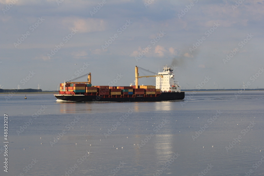 a little containerschip with cranes is sailing from antwerp towards the north sea through the westerschelde sea at a beautiful day in summer