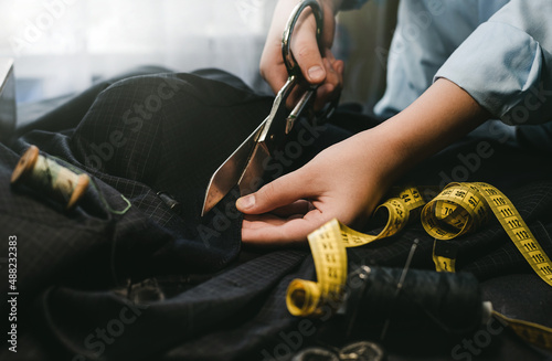The tailor's hands with scissors cut the fabric for tailoring. Cutting fabric or material