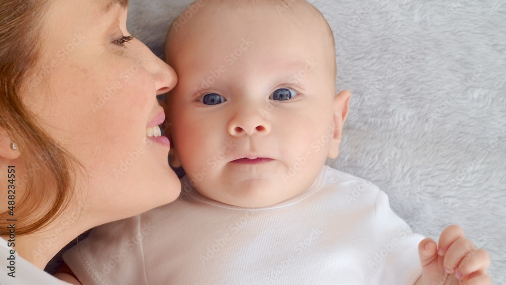 Happy newborn baby with his mother. Healthy newborn baby in a white t-shirt with mom. Closeup Faces of the mother and infant baby. Cute Infant boy and parent, top view. Happy family portrait Happy newborn baby with his mother. Healthy newborn baby in a white t-shirt with mom. Closeup Faces of the mother and infant baby. Cute Infant boy and parent, top view. Happy family portrait