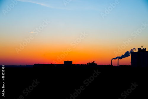 Panorama sunrise with silhouette of town with chimney and helicopter. A cityscape of buildings in the shadow under sunset with colorful sky sand light clouds in Kyiv, Ukraine.