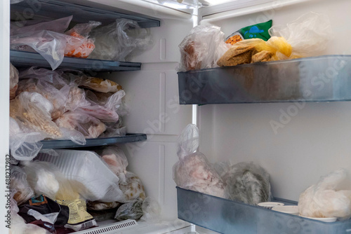 Frozen foods are in a freezer with the door open, a messy inside of a deep freezer,