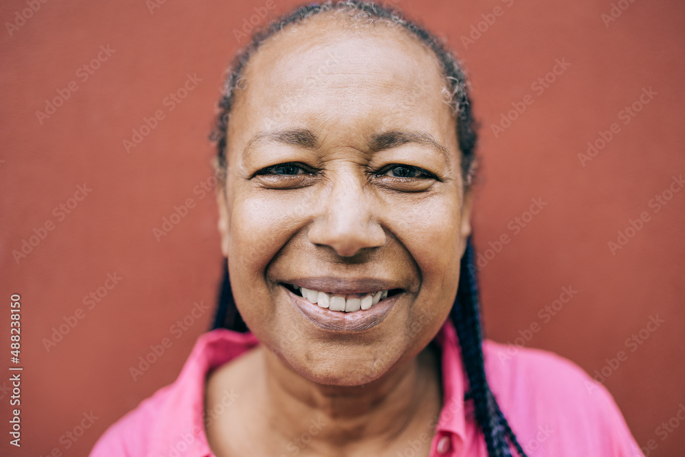 Obraz premium Happy senior African woman posing and smiling on camera outdoor - Real people, diversity and elderly concept - Focus on eyes