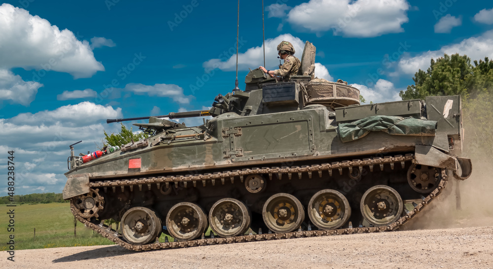 close up of a British army Warrior FV510 light infantry fighting vehicle tank in action on a military exercise, blue sky with light clouds, Wiltshire UK