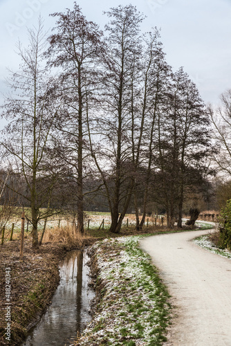 Idyllic view over the Baudouin park with a walking path along the Molenbeek creek and bare trees in winter, Belgium