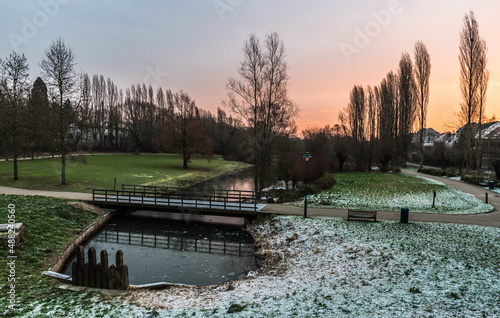 Idyllic view over a pond, bare trees and meadows covered with a thin snowlayer in the Baudouin park during sunrise, Jette Belgium photo