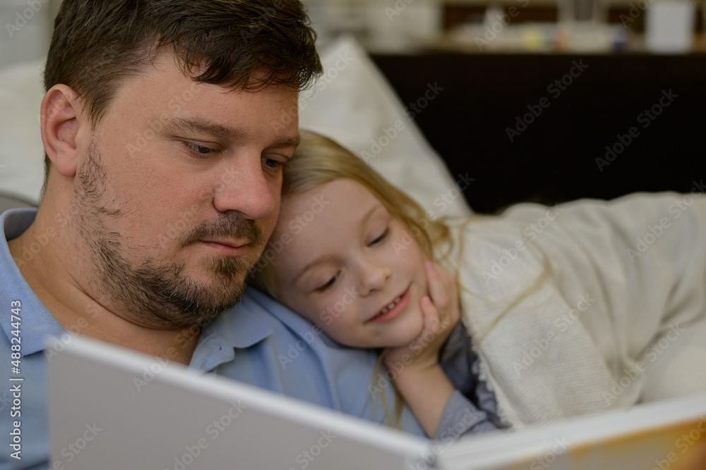 dad entertains the child during illness: he looks, reads a book, a photo book with his daughter home. The father suspects that his daughter is ill. The child is not feeling well. the concept of