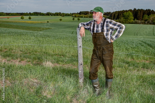 Foto A farmer with green dungarees and rubber boots has leaned against a fence post and is contemplating his dry pasture