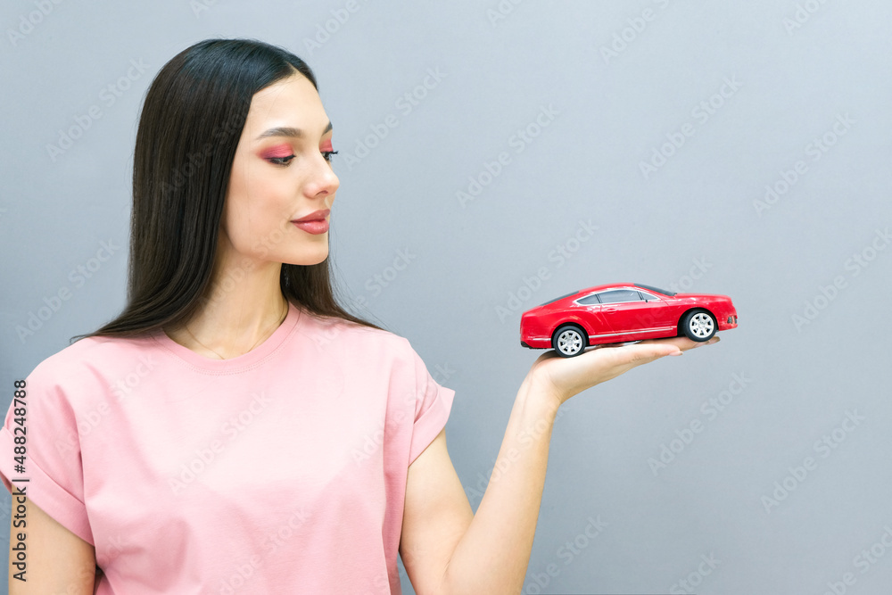 Driving school idea and concept, student driver passed the exam, drivers license, portrait of a beautiful happy young woman, holding a car in her hand. on a gray isolated background Driving school idea and concept, student driver passed the exam, drivers license, portrait of a beautiful happy young woman, holding a car in her hand. on a gray isolated background