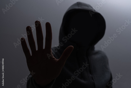 Silhouette of man in the hood or hooligan over dark background with copy space
