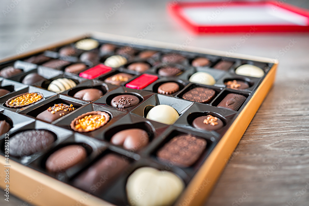 Box of chocolates truffles gourmet milk and dark sweets bonbons package with different heart shapes variety side closeup with lid in background Box of chocolates truffles gourmet milk and dark sweets bonbons package with different heart shapes variety side closeup with lid in background