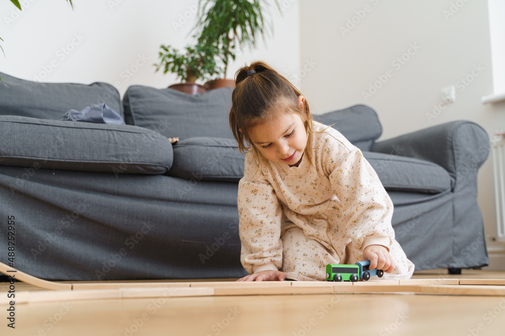 Toddler girl in white dress plays with wooden train at home in the living room Toddler girl in white dress plays with wooden train at home in the living room