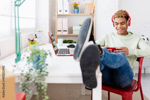 Hispanic latin young adult man playing online games on mobile phone while relaxing in his room - Entertainment and leisure concept