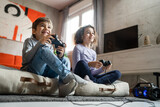 Two children small caucasian brother and sister happy children siblings boy and girl playing video game console using joystick or controller while sitting at home real people family leisure concept