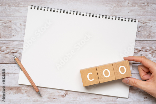 「COO」と書かれた積み木、ノート、ペン、人の手