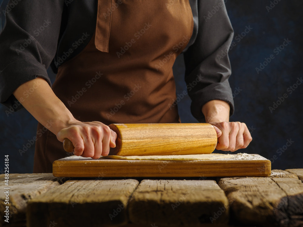 The process of preparing dough products by a professional chef. Rolls out the dough with a rolling pin on a wooden table. Close-up. Pizza, pie, pasta. Recipes for restaurant and home cooking. The process of preparing dough products by a professional chef. Rolls out the dough with a rolling pin on a wooden table. Close-up. Pizza, pie, pasta. Recipes for restaurant and home cooking.