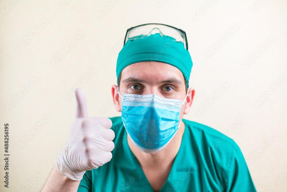 Doctor with thumb up in green surgeon suit and glasses on the yellow background isolated Doctor with thumb up in green surgeon suit and glasses on the yellow background isolated