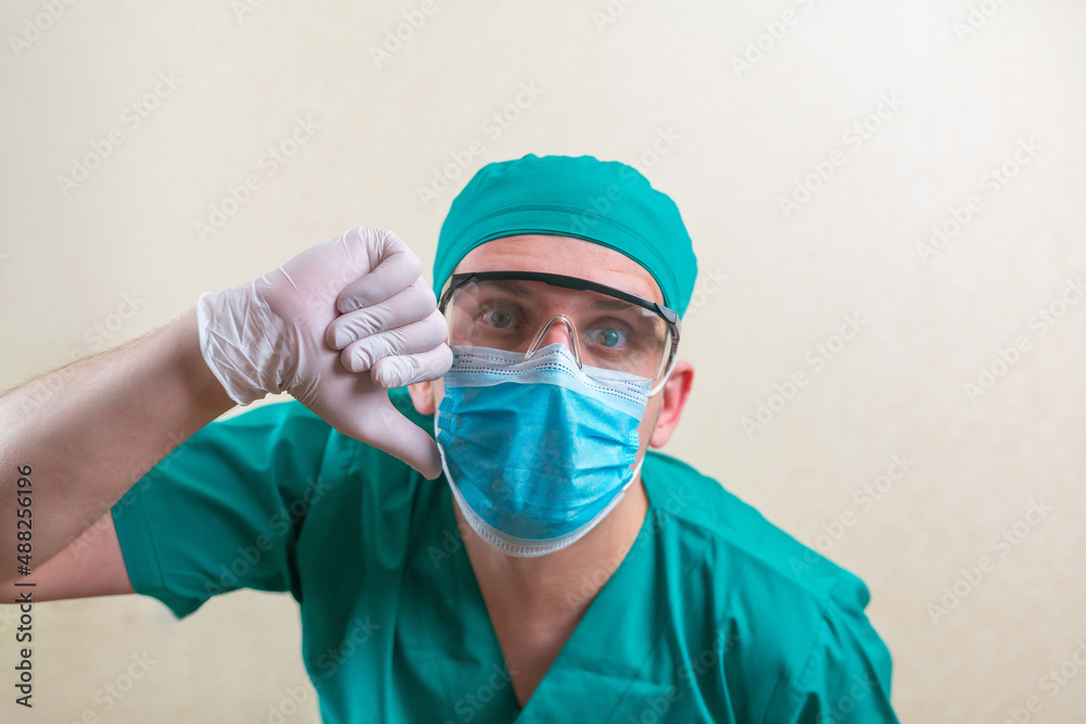 Doctor with thumb down in greensurgeon suit and glasses on the yellow background isolated