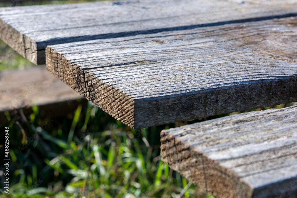 Fototapeta premium Part of a wooden table with weathered old planks in the park on a sunny spring day. Close up and copy space for text or design