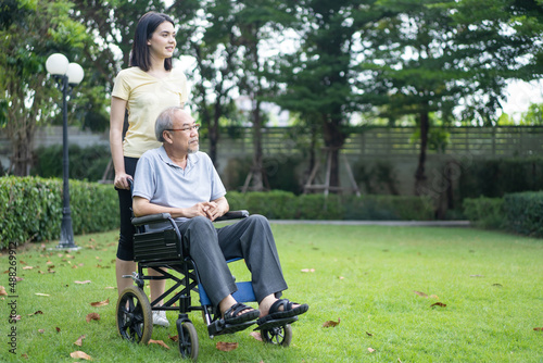 Asian senior grandfather sit on wheelchair with daughter at green park. 