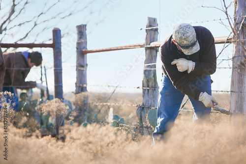 Rancher and young cowboy fixing barbed wire fence to keep livestock safe on the beef cattle ranch