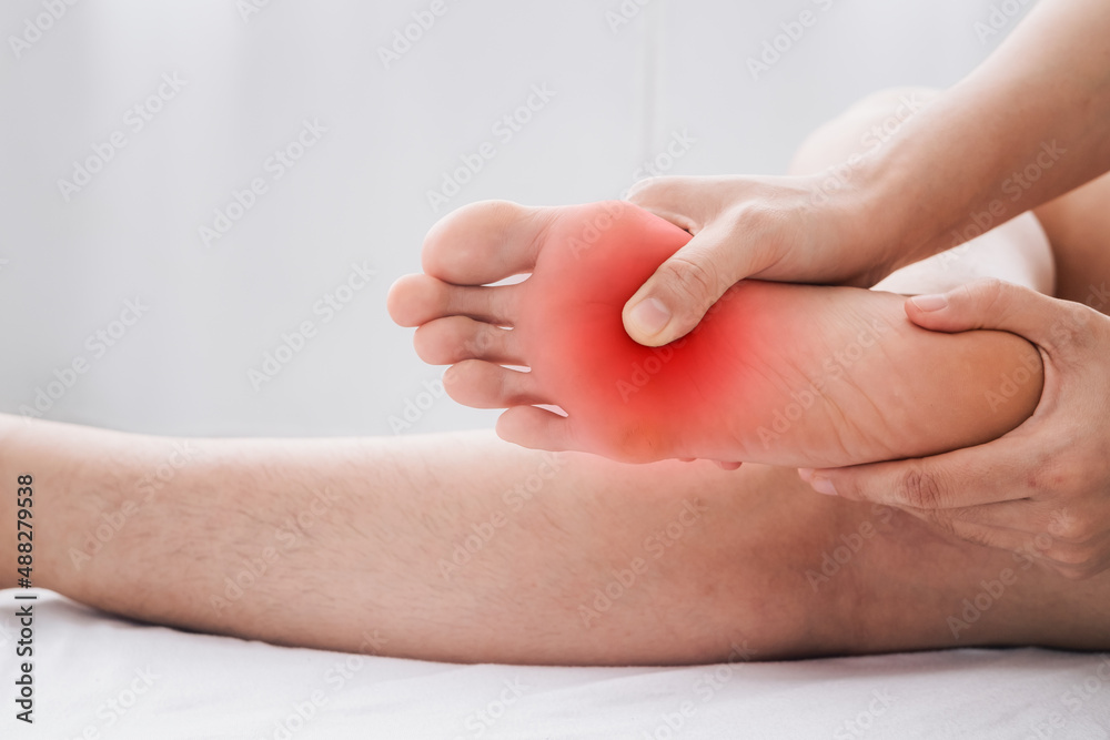 Pain in the foot, Man holds hands to his feet, foot massage, cramp, muscular spasm, red accent