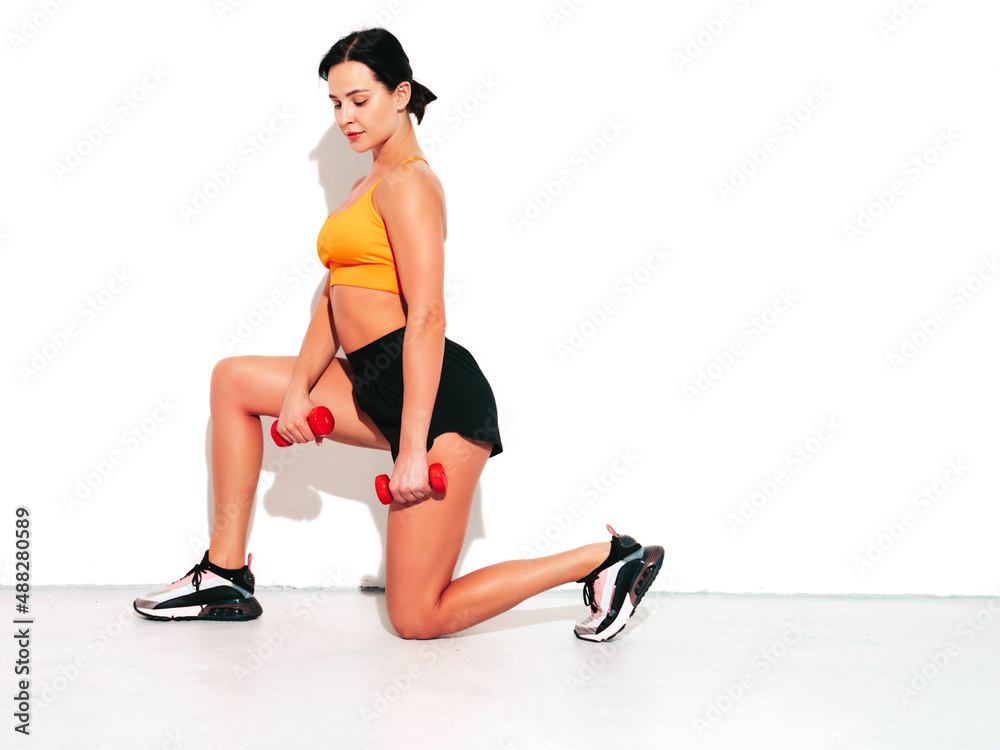 Fitness confident woman in black sports clothing. Sexy young beautiful model with perfect body. Female isolated on white wall in studio. Stretching out before training. Doing lunges with dumbbells