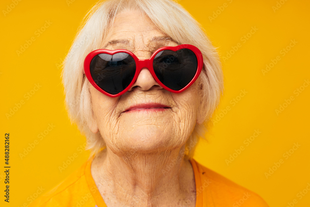 elderly woman in dark glasses in the shape of a heart yellow background elderly woman in dark glasses in the shape of a heart yellow background