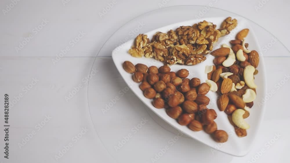 Various nuts close-up on a rotating white plate on a white wooden table. View from above. 4k raw video. Various nuts close-up on a rotating white plate on a white wooden table. View from above. 4k raw video.