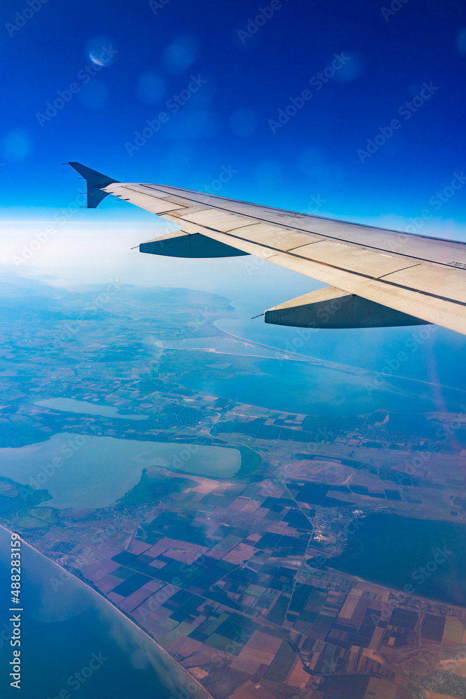 Obraz premium View from the airplane window at a beautiful blue clear sky, earth, sea and the airplane wing