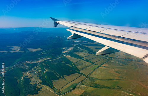 View of airplane wing, blue skies and green land during landing. Airplane window view.