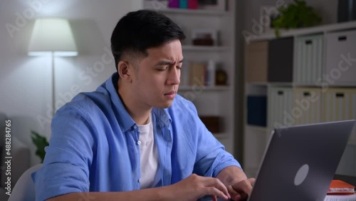 Young Asian businessman looking serious and stressed while using laptop to work from home.