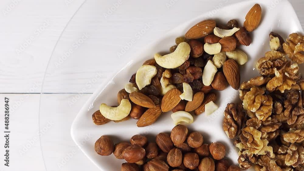Various nuts close-up on a white plate on a white wooden table. View from above. 4k raw video with smooth camera movement. Various nuts close-up on a white plate on a white wooden table. View from above. 4k raw video with smooth camera movement.
