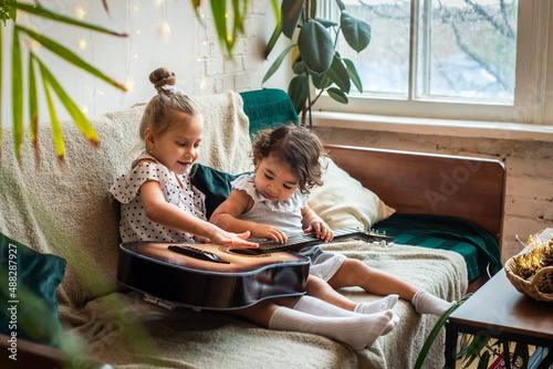 white and black girls on a couch and plays the guitar. babes is playing, composes melody and music.