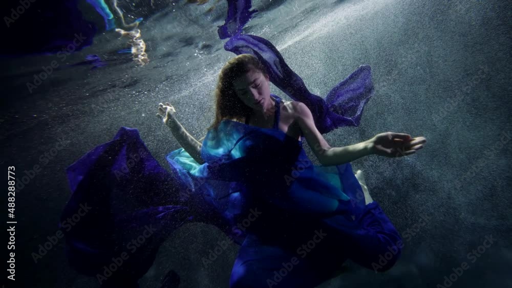 mysterious underwater world of magical lake, woman in blue dress is floating in depth