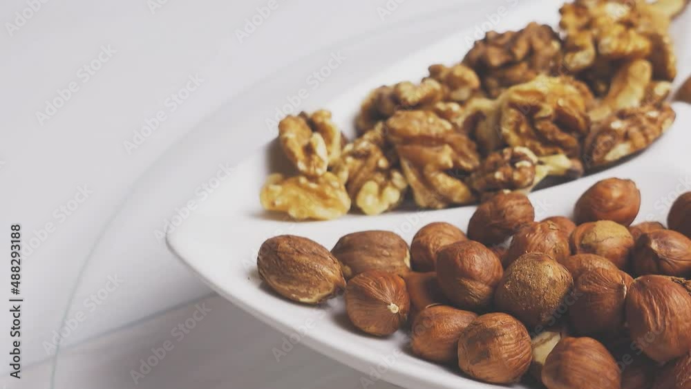 Various nuts close-up on a white plate on a white wooden table. 4k raw video with smooth camera movement. Various nuts close-up on a white plate on a white wooden table. 4k raw video with smooth camera movement.