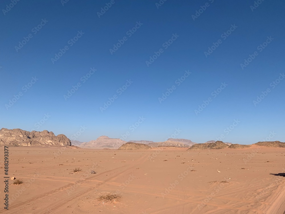 traces of cars in the sand against the background of stone cliffs in the desert; sand, rocks and blue sky