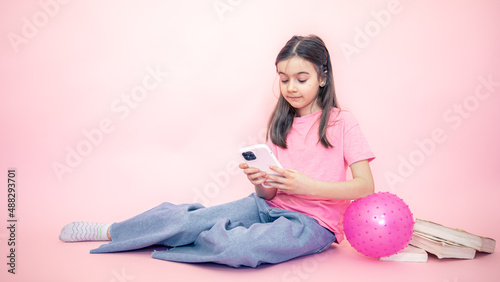 Fotografie Little girl with a smartphone in her hands on a pink background, copy space