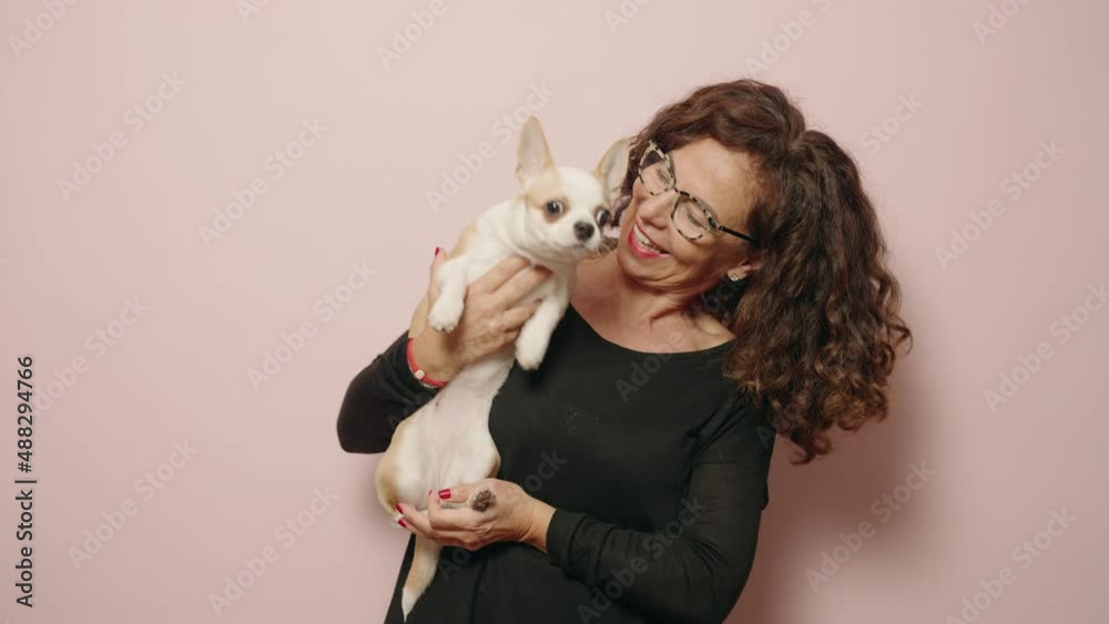 Middle age woman smiling confident hugging chihuahua over pink background Middle age woman smiling confident hugging chihuahua over pink background