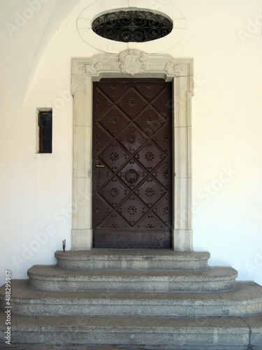 The entrance consists of a wrought-iron metal door with a white trim and gray granite steps with a porch, with an oval transom window above the entrance with a lattice.